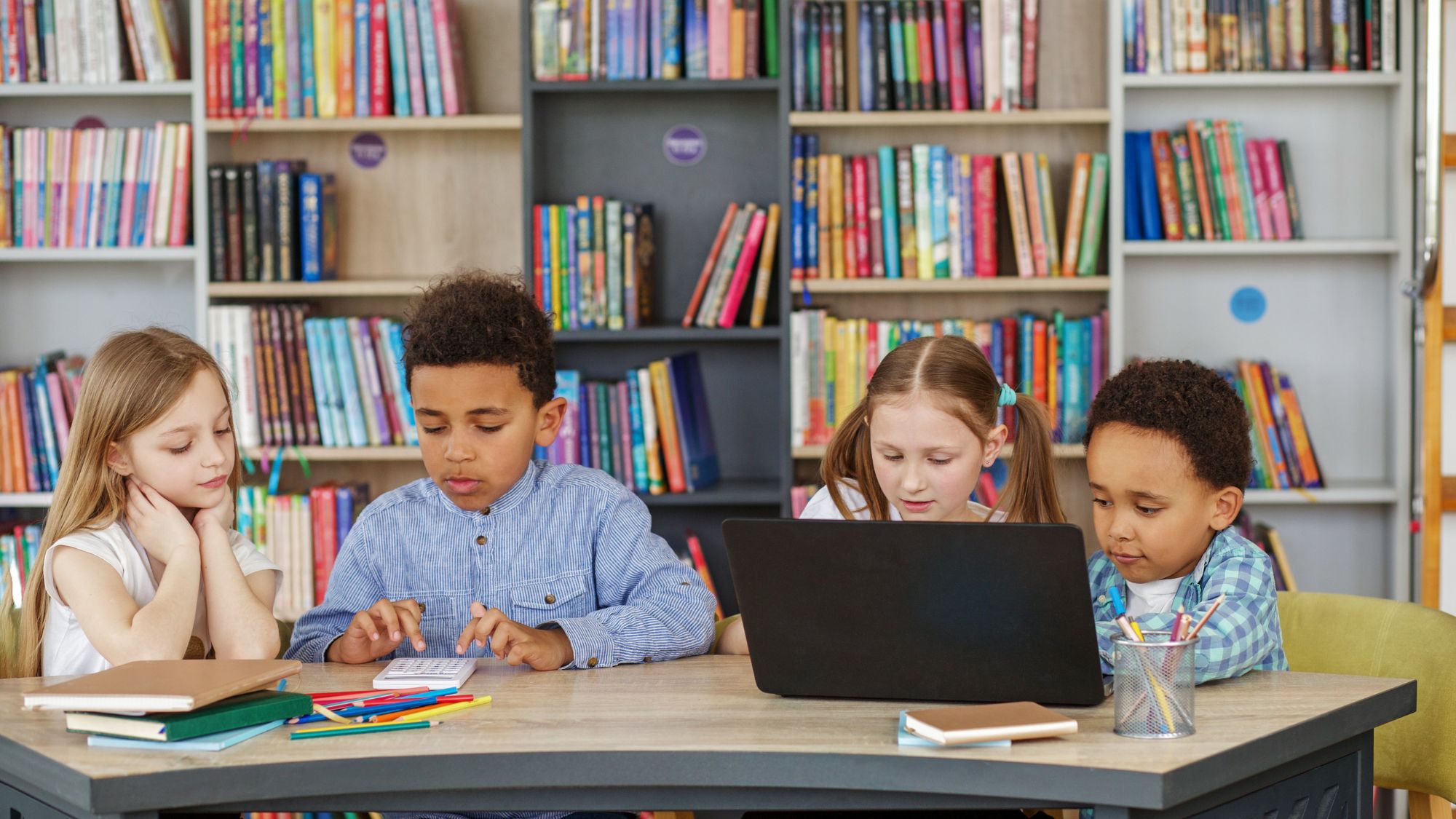 Two children reading from a laptop and two children reading from a book